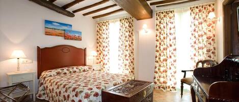 Un dormitorio con una cama de madera, una mesita de noche, una lámpara, un aparador, una silla y una ventana con cortinas florales.