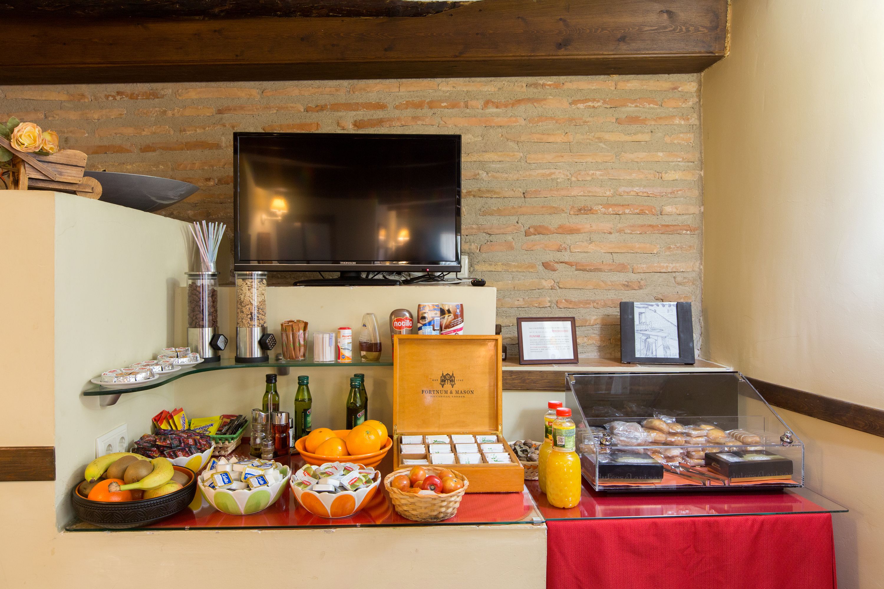 A breakfast buffet with various food items, a television, and a brick wall.