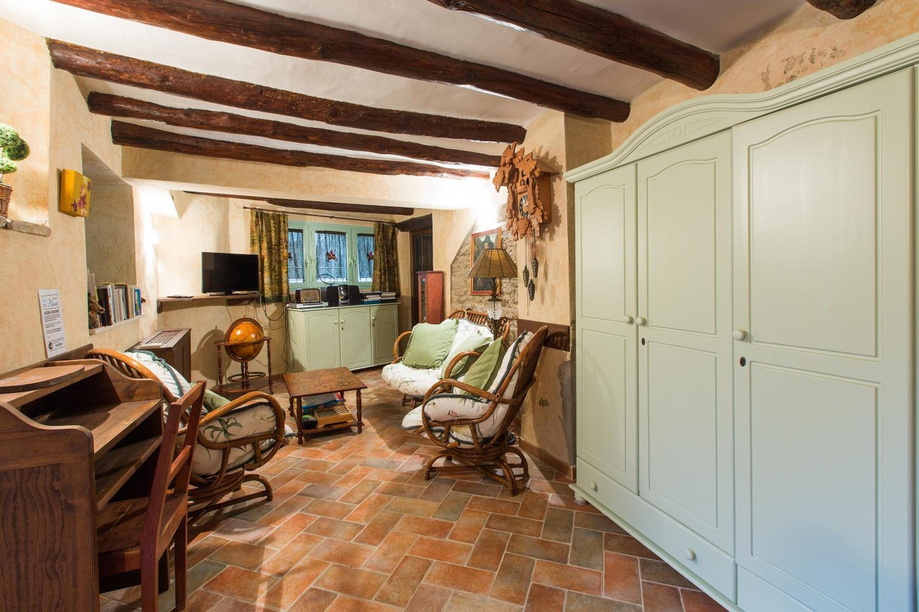 A rustic room with exposed wooden beams, a large wardrobe, a wooden desk, a globe, and a wicker chair.