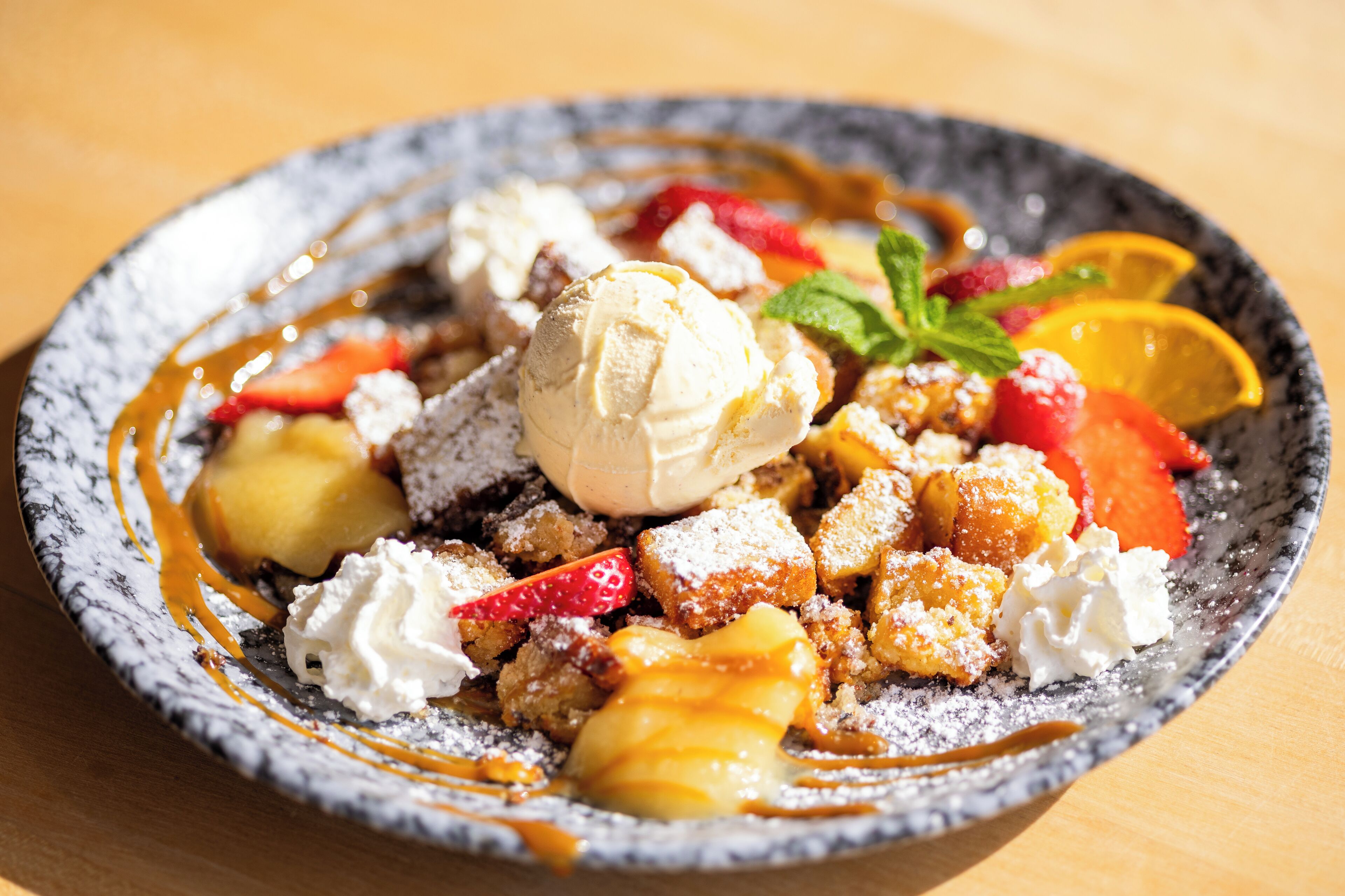 A dessert plate with ice cream, fruit, and powdered sugar.