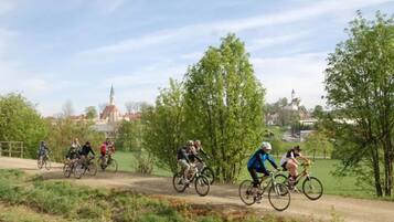 Ciclistas em uma trilha de terra, com vegetação e edifícios ao fundo.
