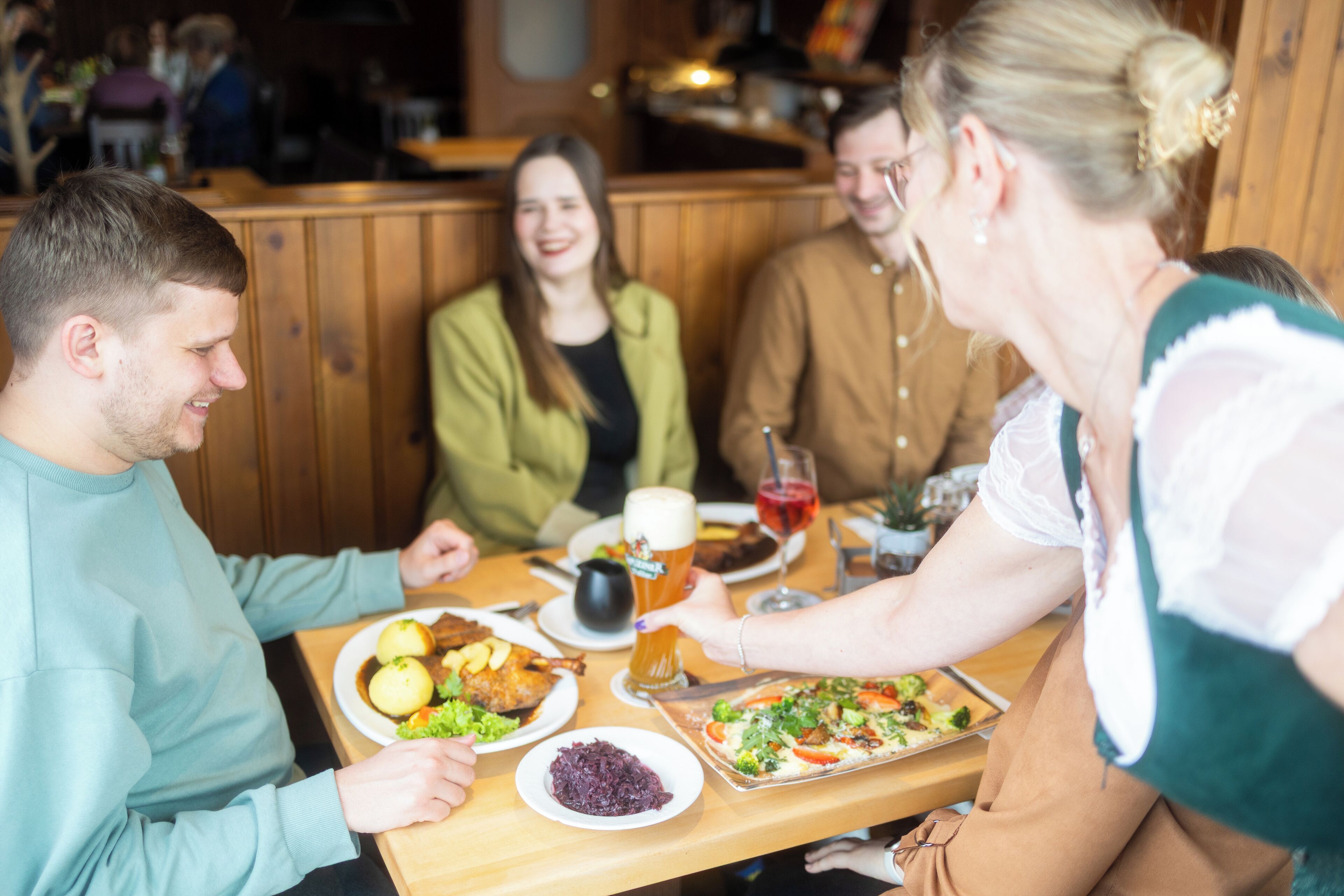 A group of people seated at a wooden table in a restaurant with a variety of dishes and drinks.