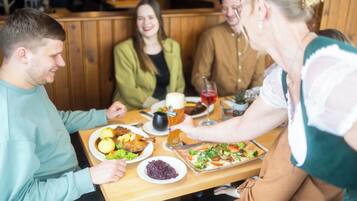 A group of people seated at a wooden table in a restaurant with a variety of dishes and drinks.