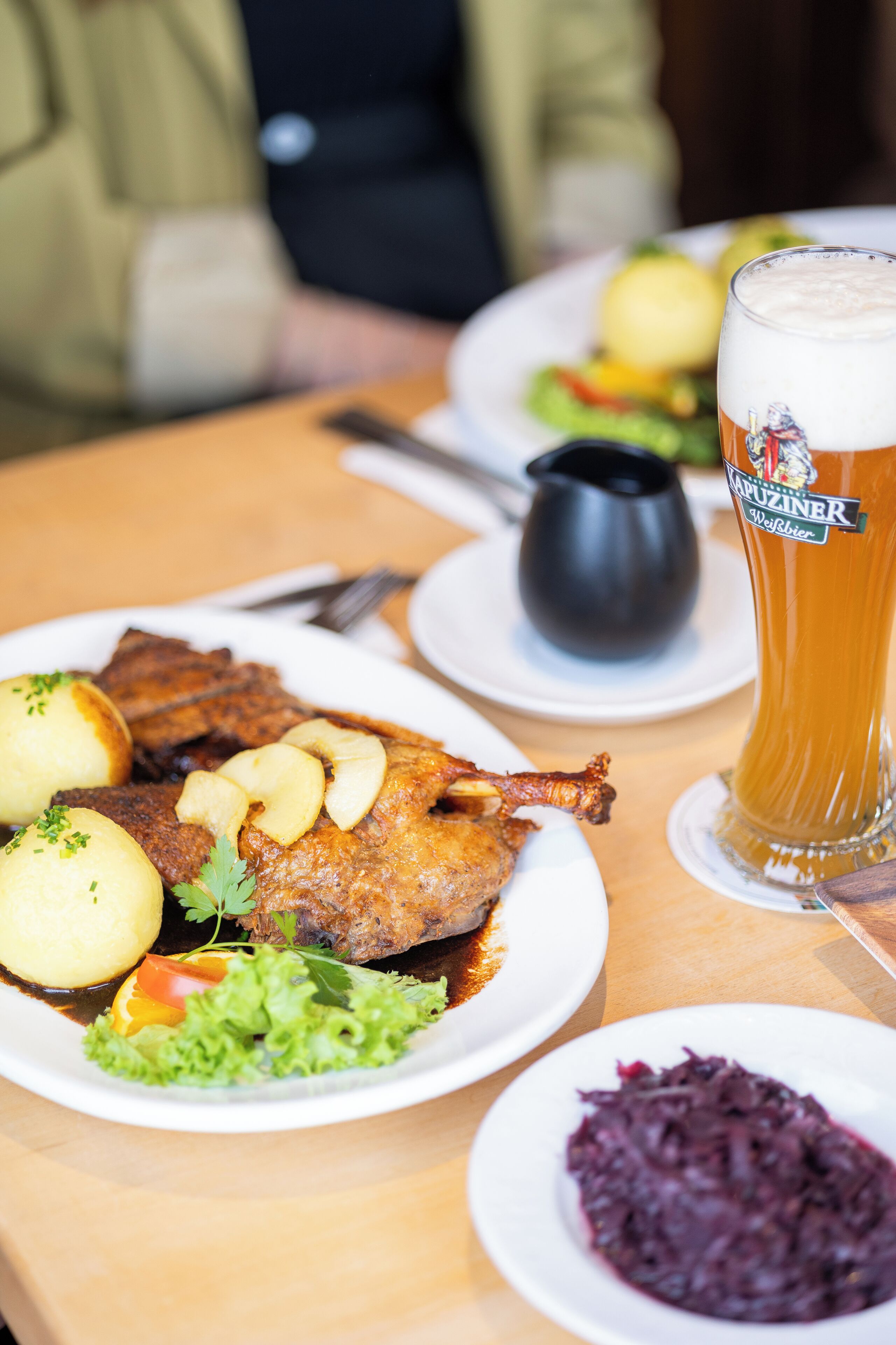 A dining table with plates of food, including a roasted duck, potatoes, and a glass of beer.