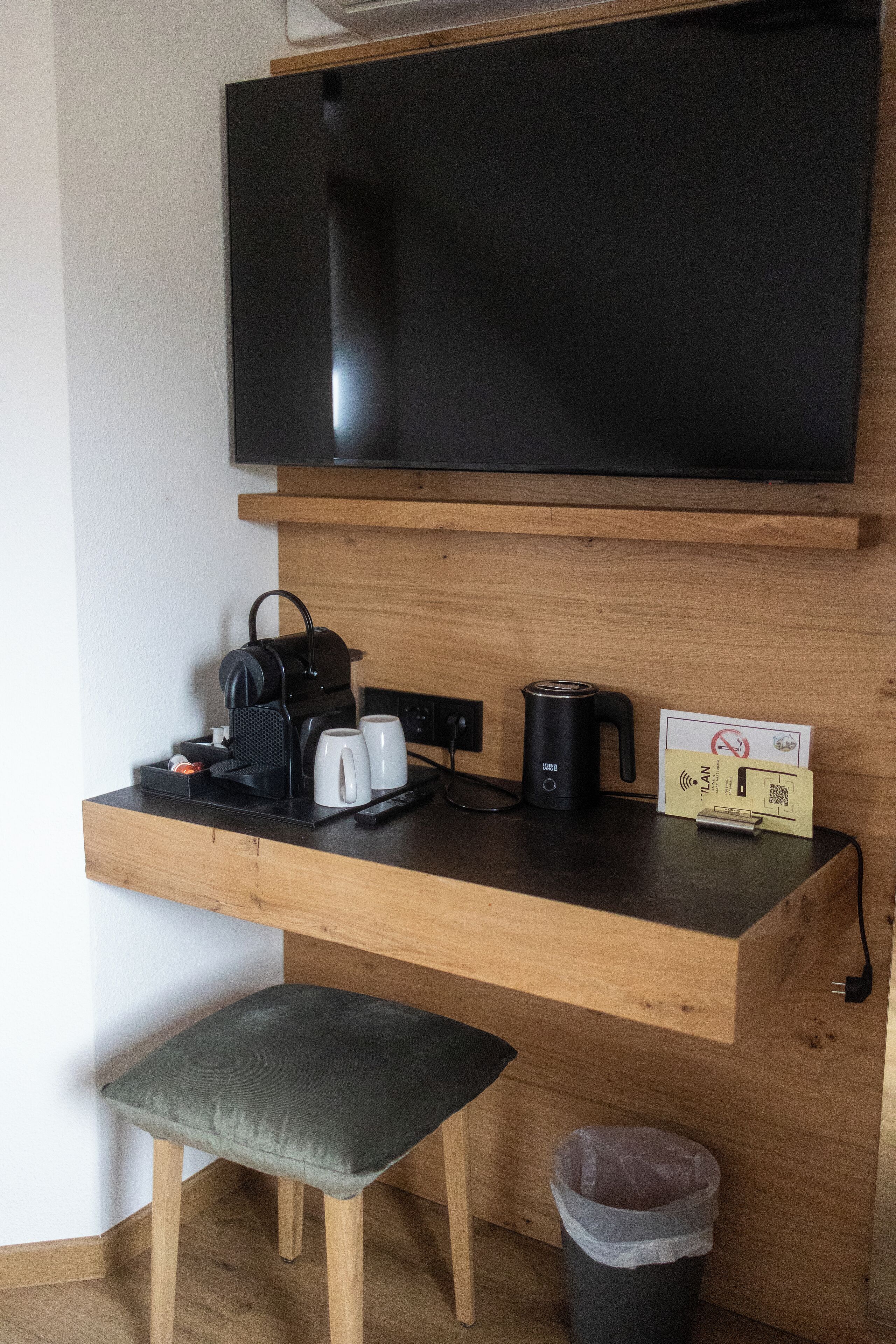 Un espacio de trabajo funcional con televisor de pantalla plana, cafetera, hervidor y estación de carga.