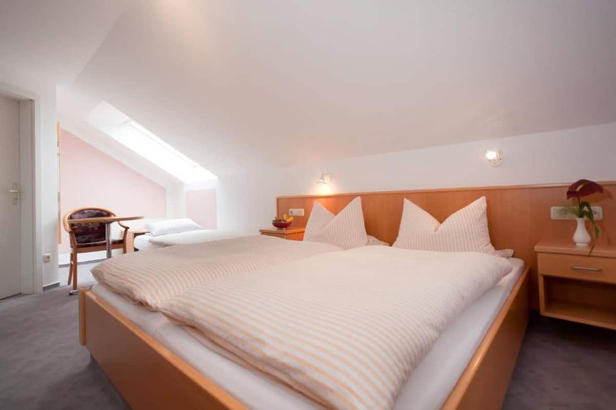 A bedroom with a large bed, a nightstand, a chair, and a skylight.