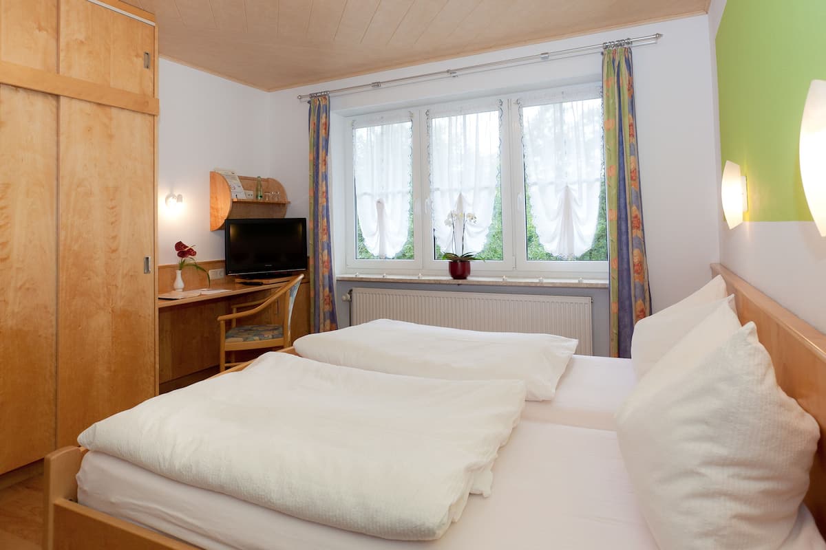 A hotel room with two beds, a desk with a television, a window with curtains, and a radiator.