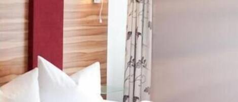A hotel room with a bed, white bedding, a red accent wall, and a patterned curtain.