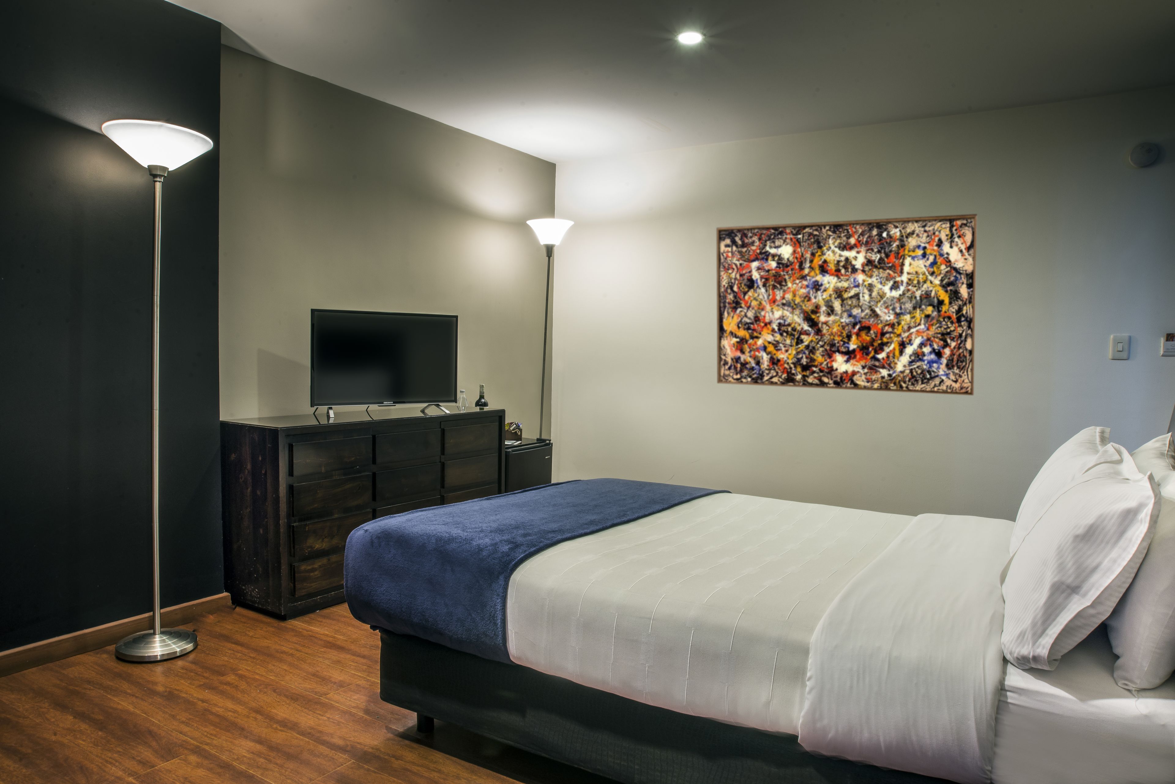 A modern bedroom with a bed, a dresser, a flat-screen TV, and a large abstract painting on the wall.
