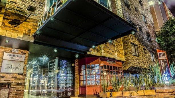 Un hôtel à la façade en briques, doté d’une entrée en verre et d’une enseigne indiquant qu’il s’agit d’une trattoria.