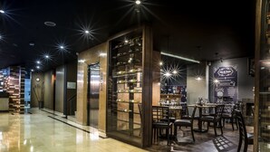 L’intérieur d’un restaurant moderne se caractérise par un sol ciré, des étagères en bois où sont exposées des bouteilles, et un espace repas avec des tables et des chaises.