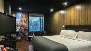 Une chambre d’hôtel équipée d’un lit, d’une télévision, d’un bureau avec une chaise et d’une fenêtre donnant sur un pont et des arbres.