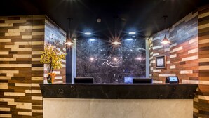 Un comptoir d’accueil avec un plateau en marbre, des panneaux muraux en bois et des luminaires suspendus.