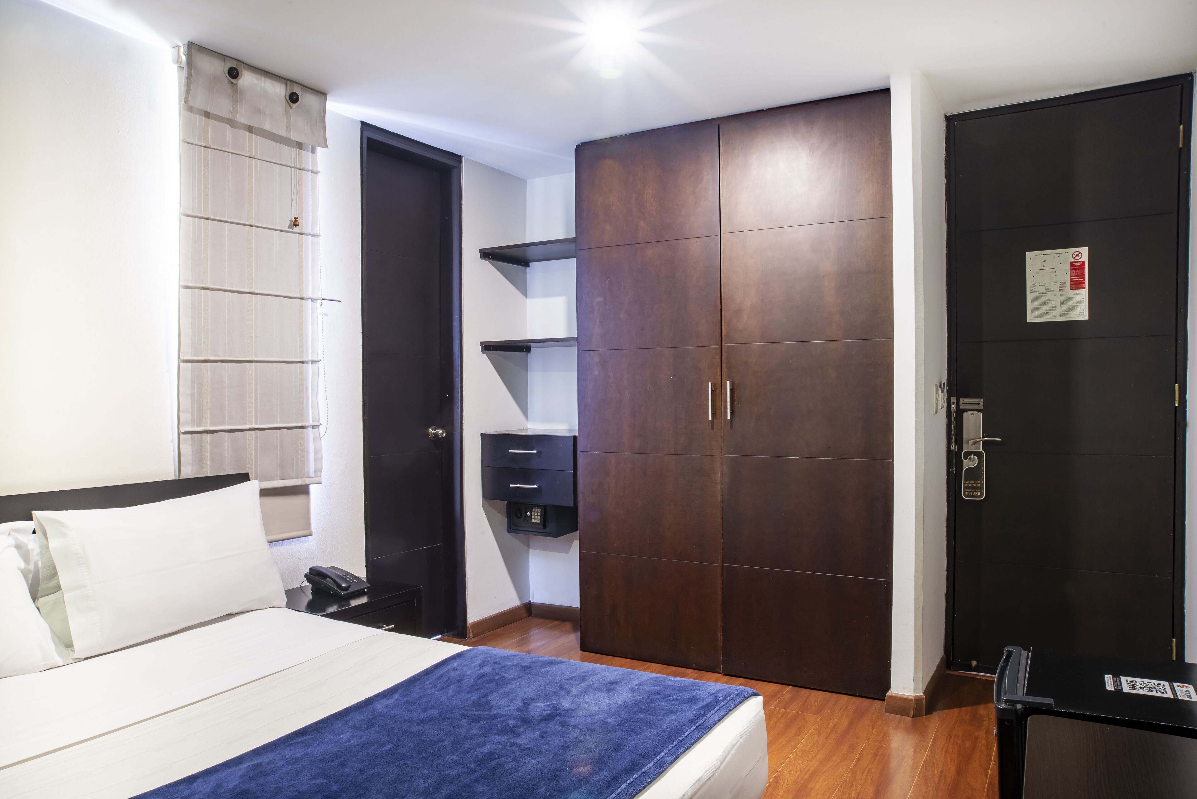 Een slaapkamer met een bed, een kledingkast, een bureau en een deur met een bordje.