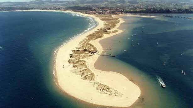 An aerial view of a coastal area with a sandy beach, a curved bay, and several boats. - Hotel Estrella del Alemar (Ribamontan al Mar)