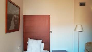 A bedroom with a wooden headboard, a bed with white linens, a nightstand, a floor lamp, and a chair.