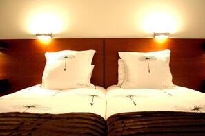A hotel room with a mirrored wall design, two bedside lamps, and a bed with a white duvet featuring a dandelion pattern.
