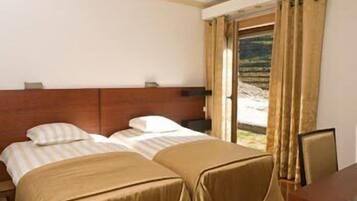 A hotel room with two beds, a wooden headboard, a desk, and a window with curtains.