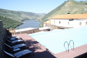 A pool area with lounge chairs and a view of a river and hills.
