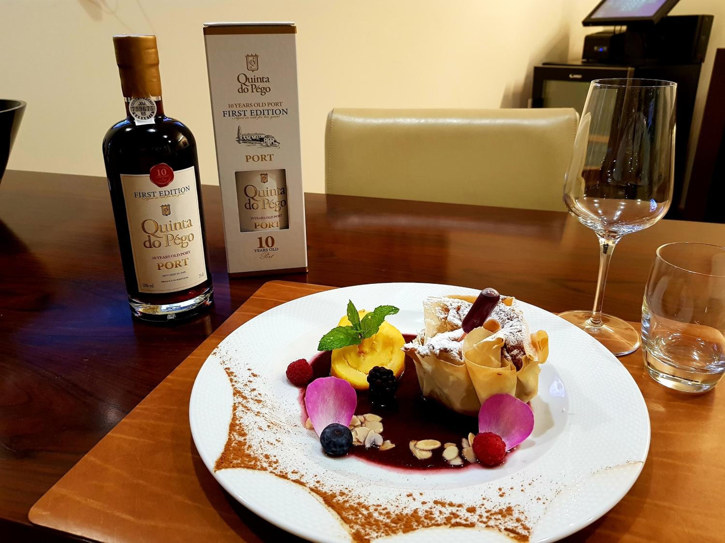 Una bottiglia di Porto Quinta do Pêgo, decennale, una scatola con l'etichetta corrispondente e un piatto da dessert con frutta e noci assortite.