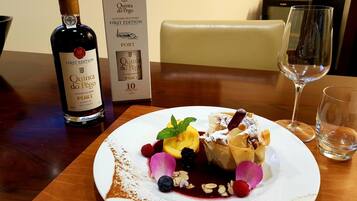 Una bottiglia di Porto Quinta do Pêgo, decennale, una scatola con l'etichetta corrispondente e un piatto da dessert con frutta e noci assortite.