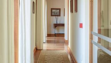 Un couloir d’hôtel avec un plancher en bois, un tapis à motifs floraux et une porte en verre sur la droite.