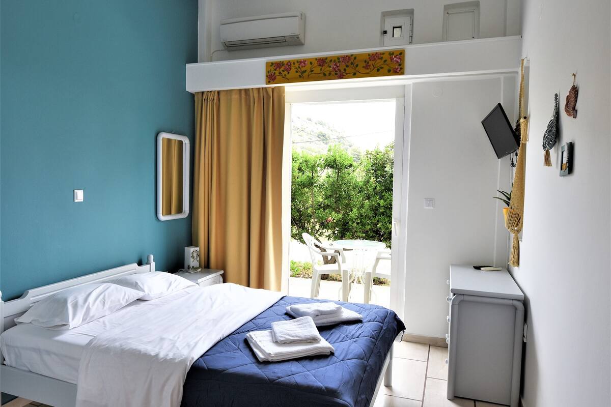 Ein Schlafzimmer mit Bett, Schreibtisch und Blick auf Grünfläche.