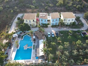 A residential area with a swimming pool, multiple houses, and parked cars.