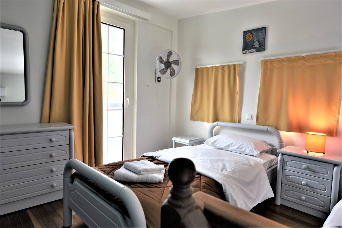 Ein Schlafzimmer mit Bett, Nachttischen, einem Schminktisch und einem an der Wand befestigten Ventilator.