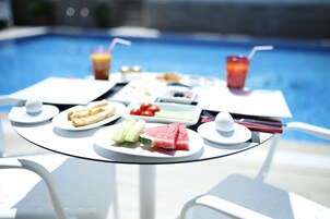 Una mesa con diversos alimentos, como sándwiches, frutas y bebidas, con una piscina al fondo.