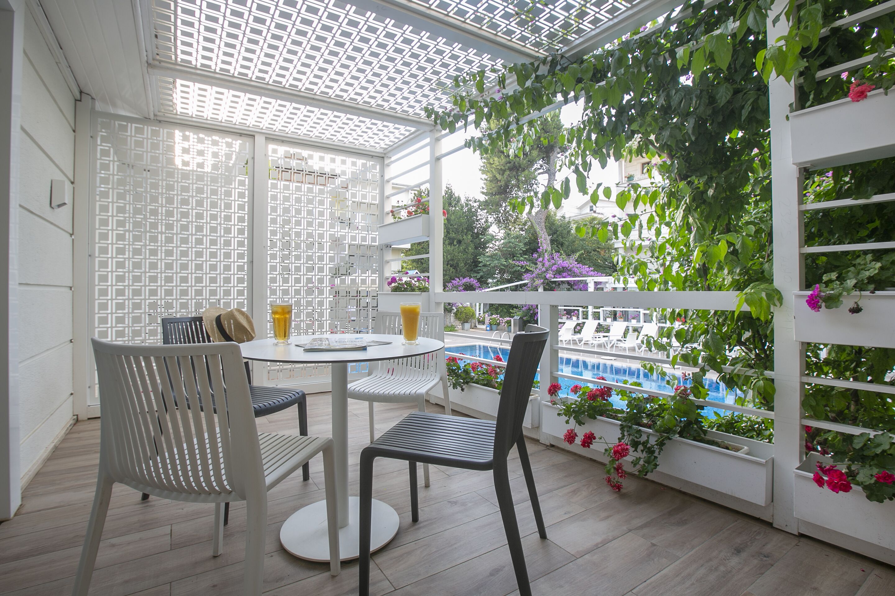 A covered patio with a pool view, white lattice partition, and outdoor seating.