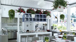 A modern kitchen with white cabinets, a central island with bar stools, and hanging flower baskets. - Ascot Hotel Buyukada (Adalar)