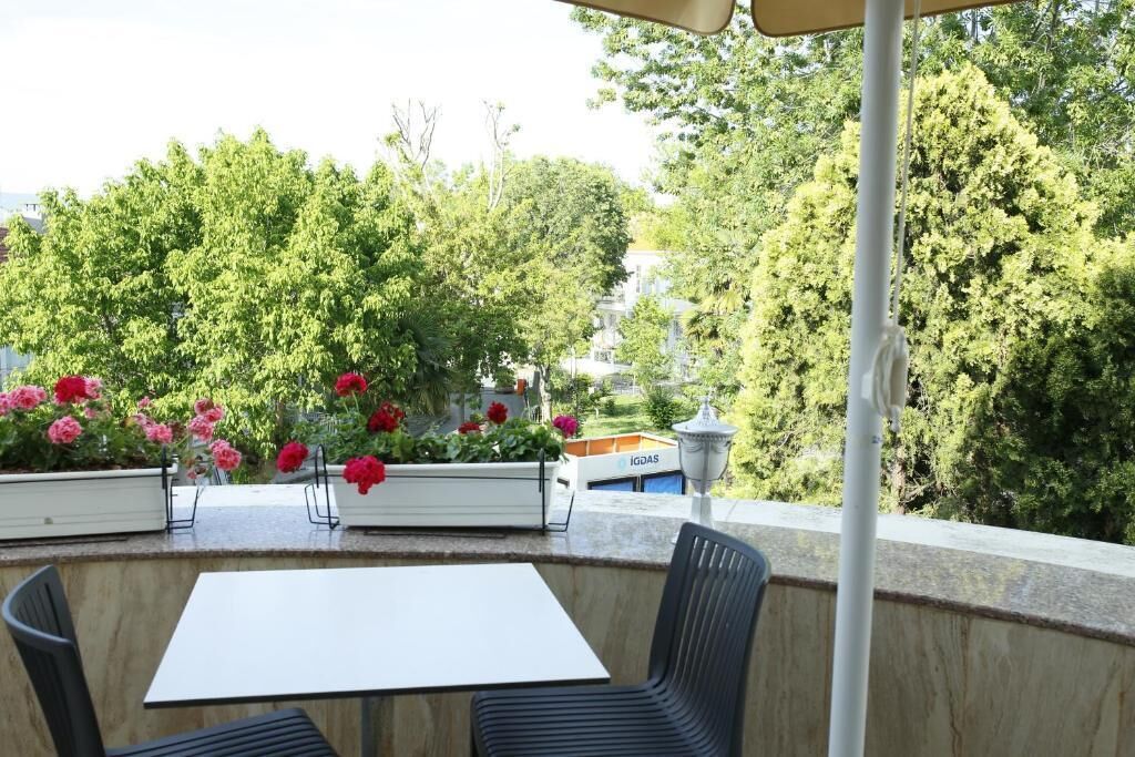 Ein Sitzbereich im Freien mit Tisch und Stühlen, umgeben von Blumenkästen und Blick auf Bäume und Gebäude.