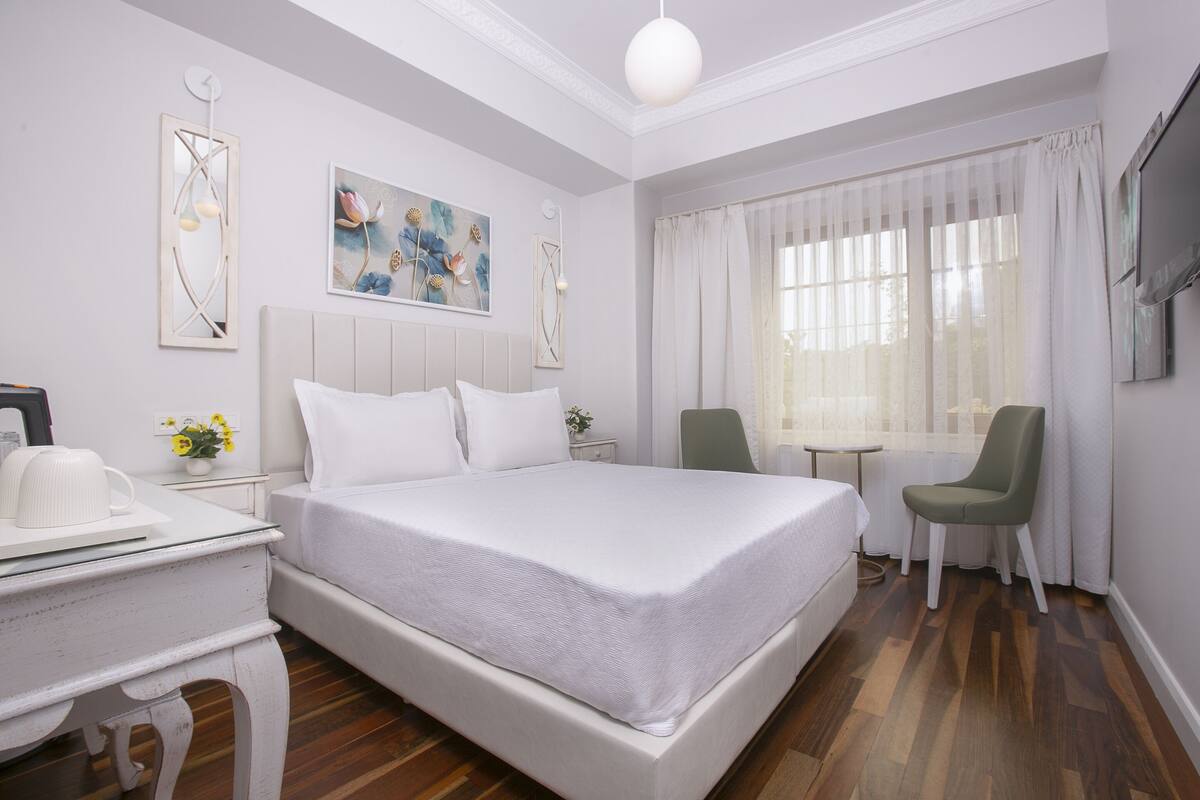 A hotel room with a large bed, a desk with a chair, a small table, and a TV.