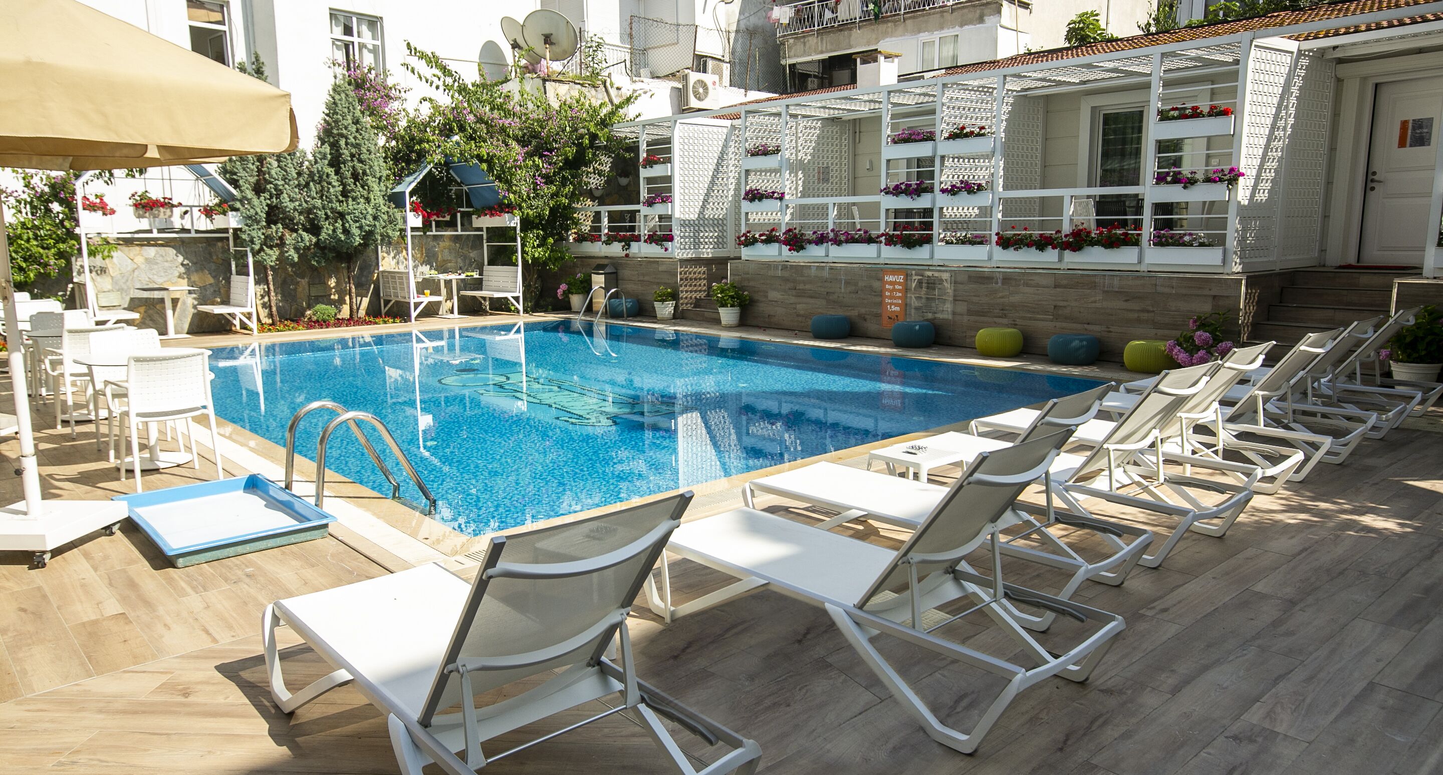 A swimming pool with sun loungers, a small table, and a covered seating area with potted plants.