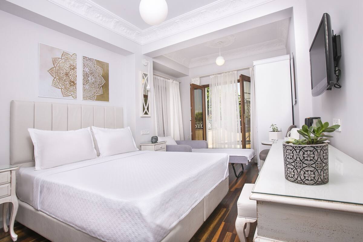 A hotel room with a large bed, bedside tables, a desk, a potted plant, and a TV mounted on the wall.