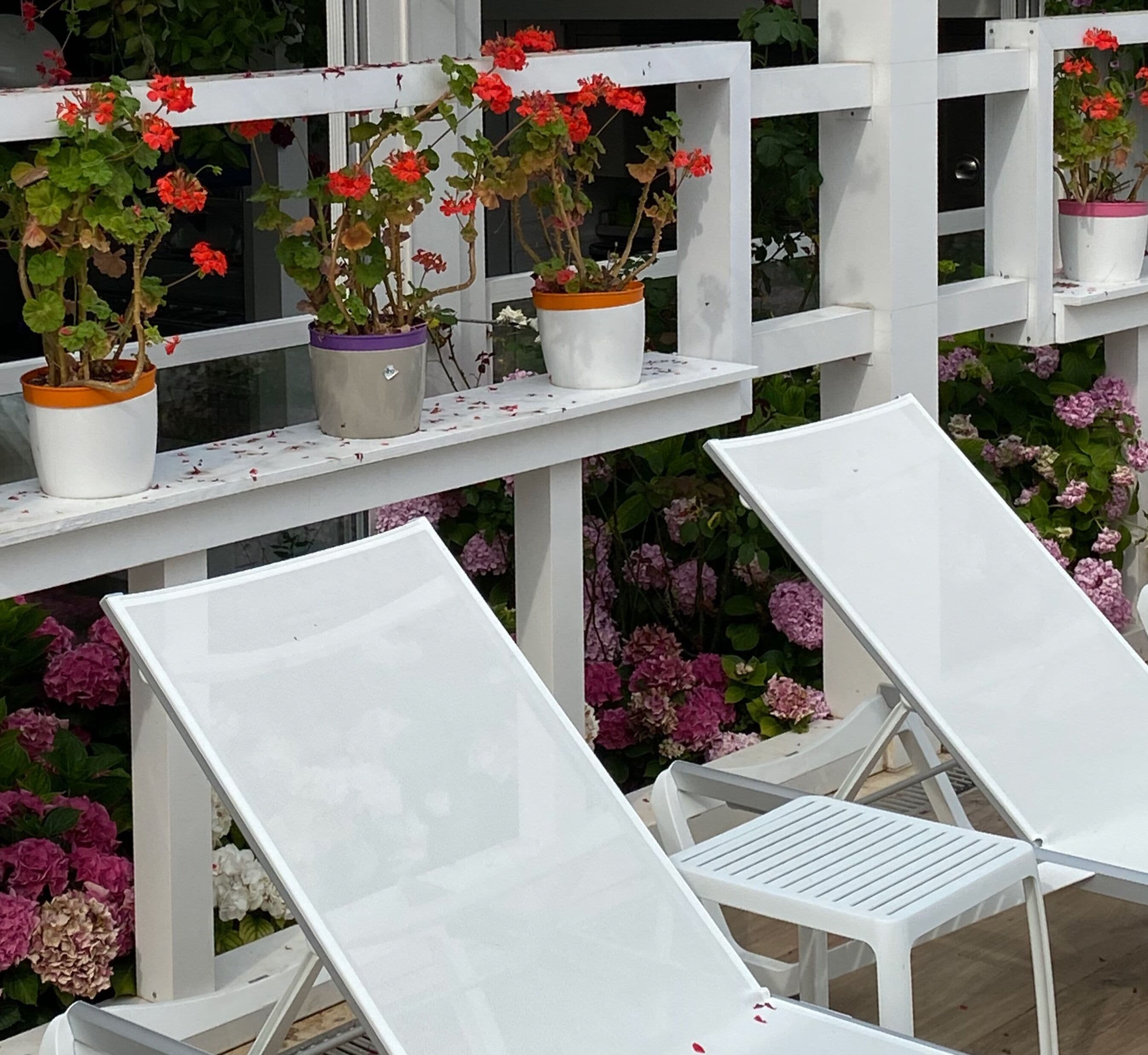 Outdoor lounge chairs with white cushions and metal frames, arranged on a white wooden deck.