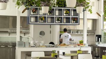 Un restaurante moderno con una barra central, plantas colgantes y un cocinero preparando comida.