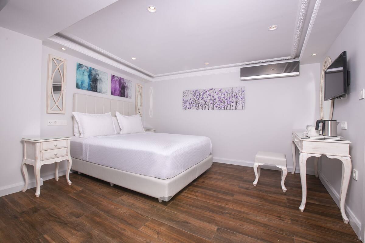 A bedroom with a bed, nightstands, a TV, and artwork on the walls.