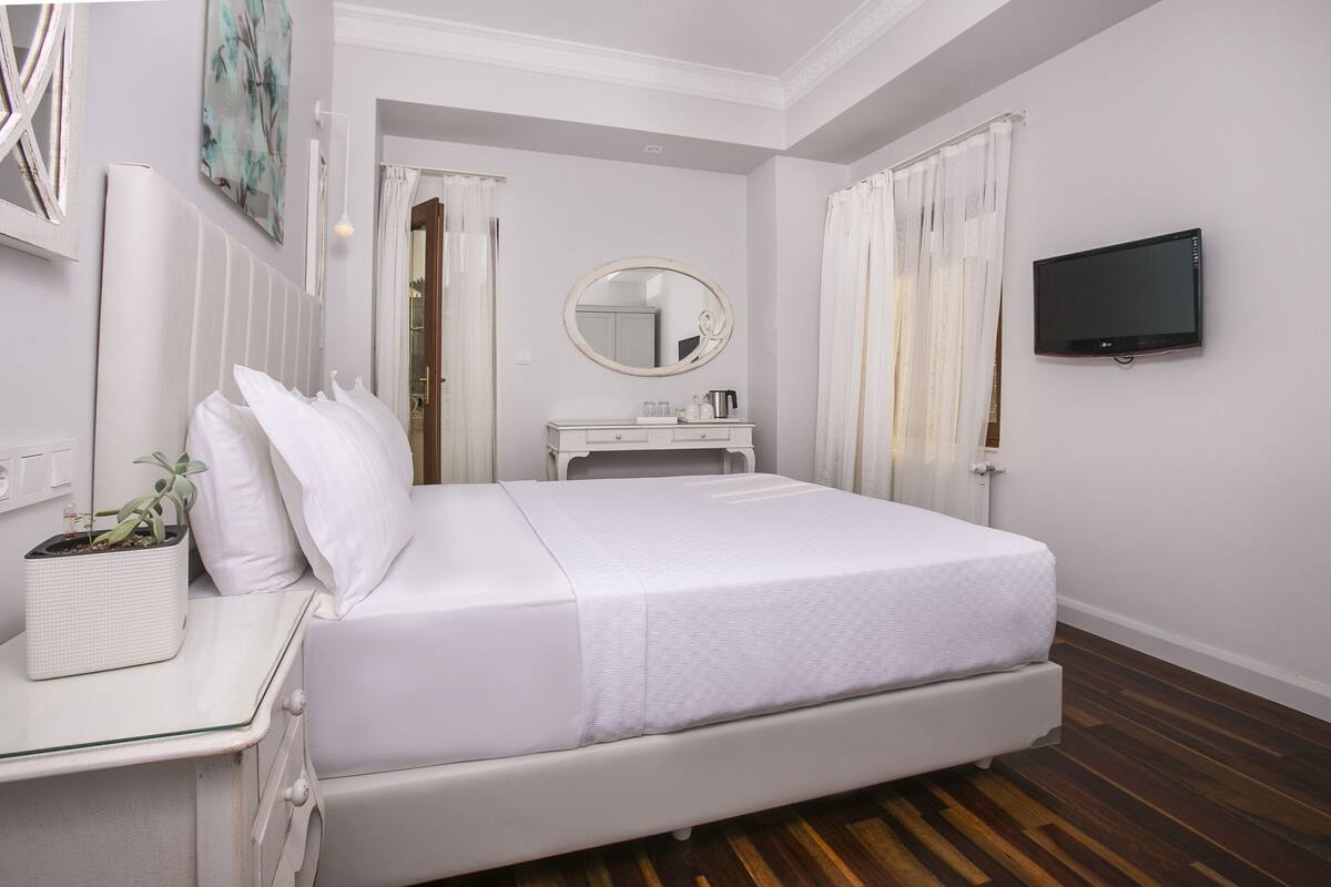 A bedroom with a bed, bedside table, mirror, and a TV on the wall.