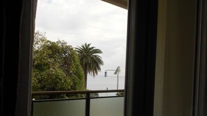 A balcony with a view of a palm tree and a building across the water. - Hotel Le Roi (Varazze)