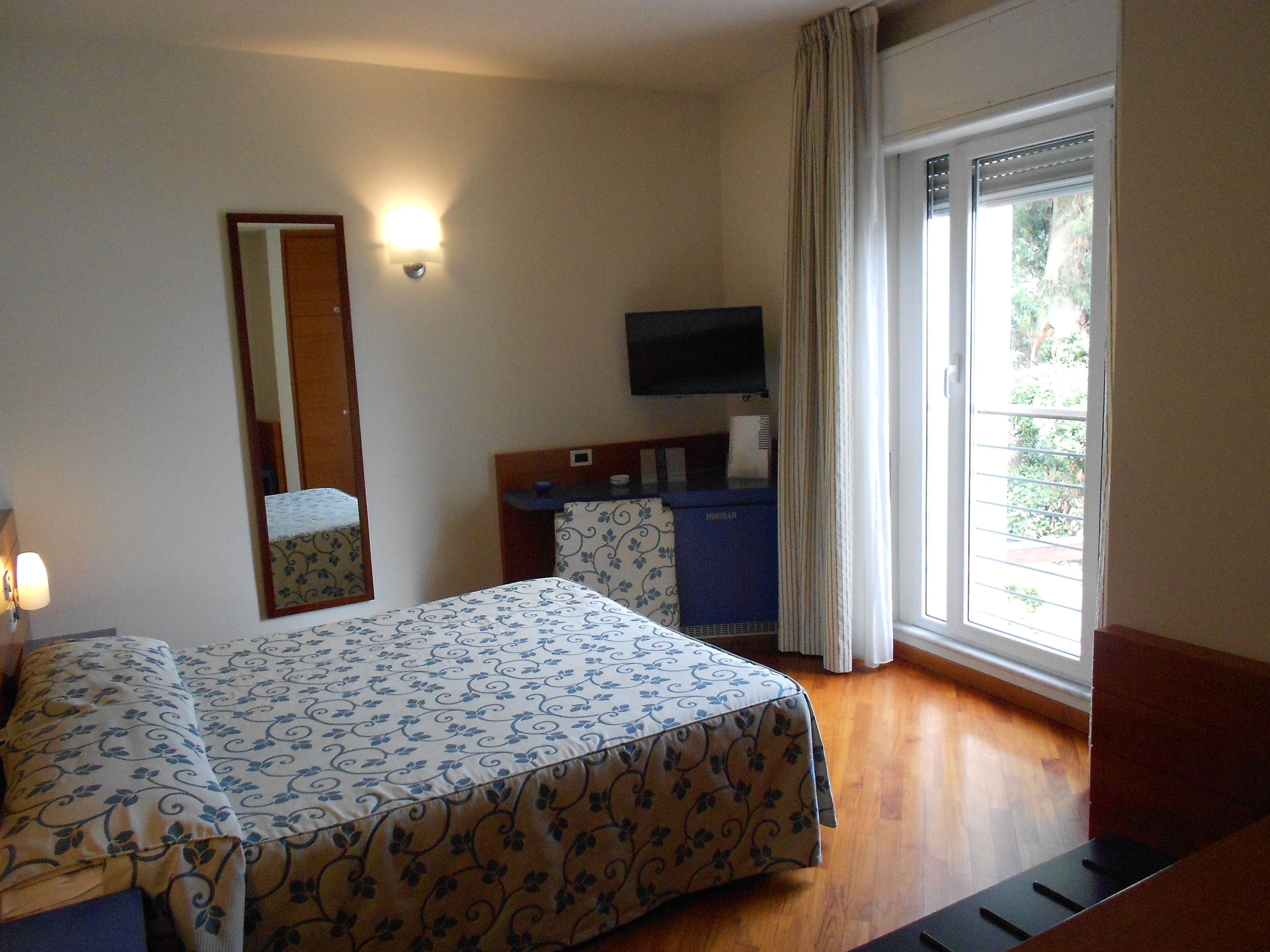 Een hotelkamer met een bed, een bureau, een televisie en een raam met gordijnen.
