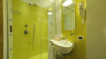 Un baño con paredes de azulejos amarillos, cabina de ducha de vidrio, lavamanos y espejo.
