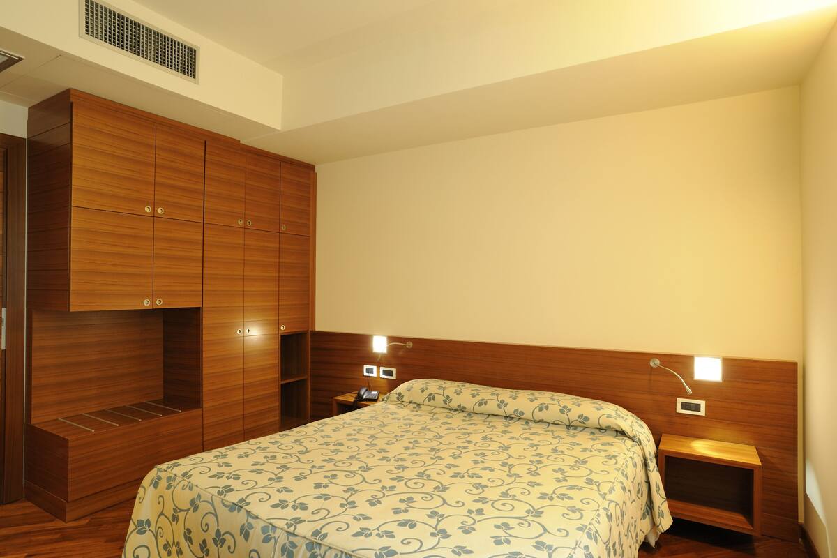 A bedroom with a large bed, wooden wardrobe, bedside tables, and a nightstand.