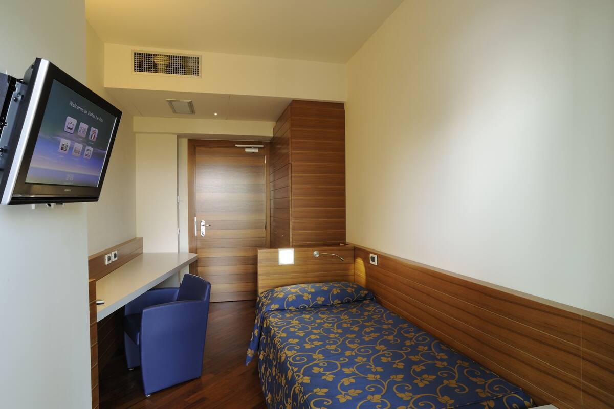 A hotel room with a bed, a desk, and a TV mounted on the wall.