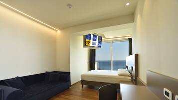 A hotel room with a bed, a sofa, a desk, and a TV displaying hotel information.