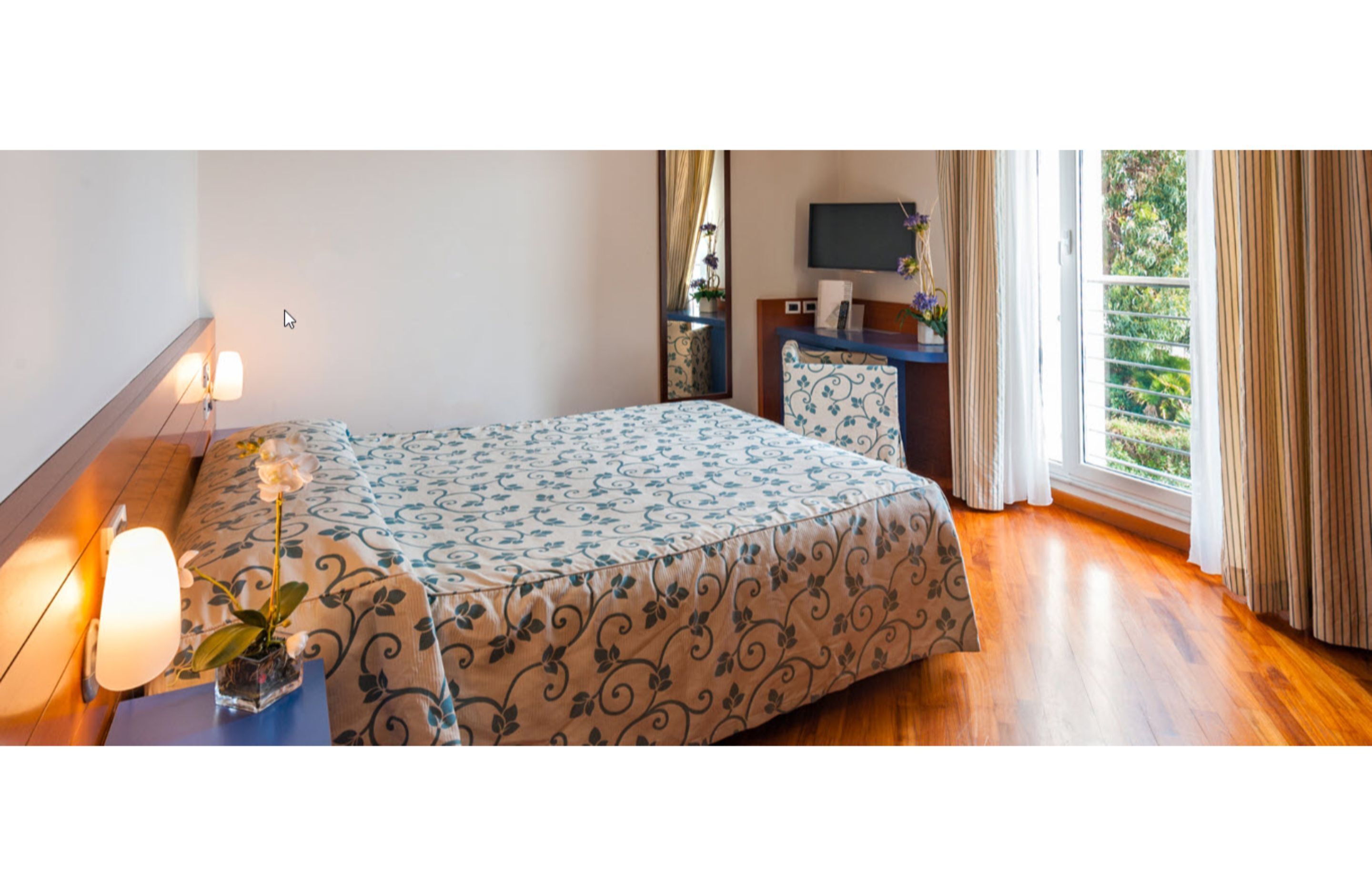 A bedroom with a bed, bedside table, lamp, and a TV on a stand.