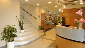 A reception area with a curved reception desk, a staircase, and potted plants. - Hotel Le Roi (Varazze)