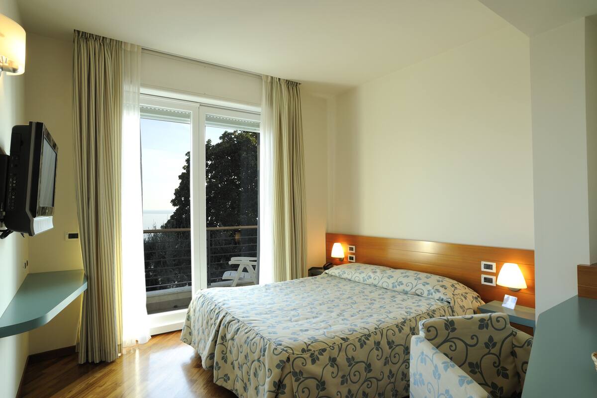A hotel room with a bed, bedside lamps, a TV, and a window with curtains.