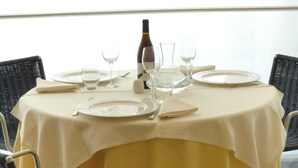 A dining table set for four with a yellow tablecloth, four chairs, and wine glasses and a bottle. - Hotel Le Roi (Varazze)